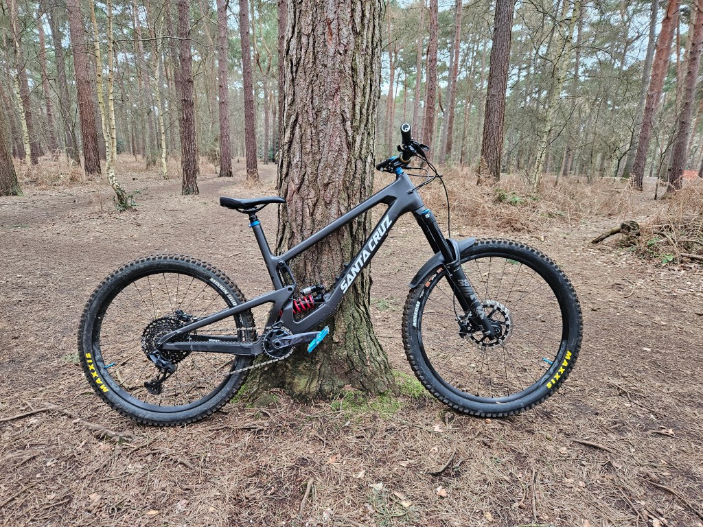 Black Santa Cruz Nomad mountain bike leaning on a tree in a forest