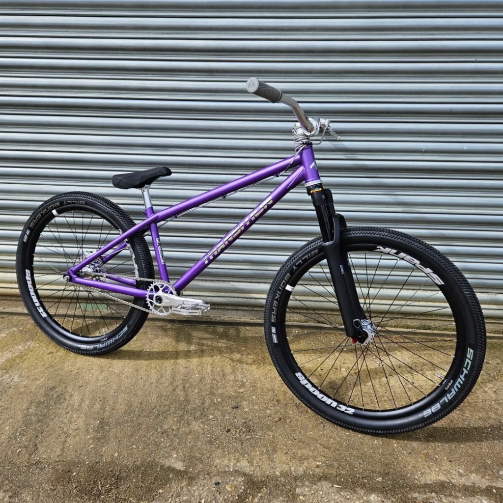 Purple Transition PBJ jump bike leaning on a metal shuttered door.